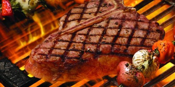 52f19c35-c949-44e9-a258-94d73198725a T-Bone steak on flaming grill framed by skewers containing red potatoes, white onions, tomatoes and sprigs of rosemary, flames shot with long exposure so they blur into a pretty orange-red