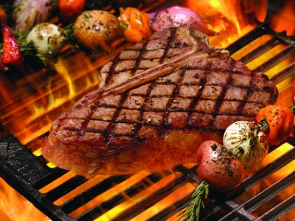 52f19c35-c949-44e9-a258-94d73198725a T-Bone steak on flaming grill framed by skewers containing red potatoes, white onions, tomatoes and sprigs of rosemary, flames shot with long exposure so they blur into a pretty orange-red